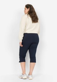 Jūriniai trumpi leggingai derinami su kremine megzta palaidine. Leggingai turi lygią tekstūrą ir yra prigludusio dizaino, siekiantys iki vidurio blauzdos.