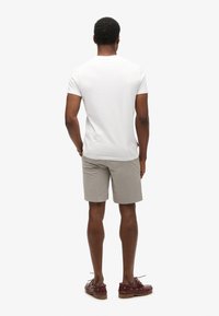 Hvid kortærmet t-shirt, lyse khaki shorts, brune bådsko, set fra ryggen. Simpelt design, afslappet pasform, ensfarvede farver, ingen mønstre.