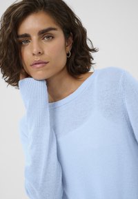 Svetlo modrý sveter z jemného pleteného materiálu, s výstrihom v tvare lode a rebrovanými manžetami. Dizajn ponúka uvoľnený strih s jemnou textúrou.