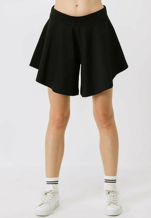 Black skort with a flared design, featuring a wide waistband and soft fabric. Paired with white sneakers and striped ankle socks.