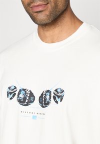 T-shirt de algodão branca com um design gráfico de quatro dados em preto e azul, com o texto "HISTORY MAKERS" e "CITY" abaixo.