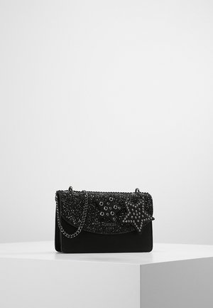 Czarna błyszcząca kopertówka z srebrnymi ćwiekami w kształcie gwiazdek i łańcuszkiem, wyeksponowana na białym postumencie na jednolitym tle.