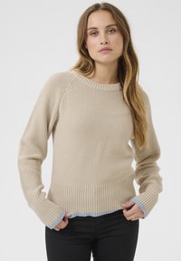 Beige neulepaita, jossa on ribatut helma ja hihansuut. Ihastuttava teksturoitu pinta ja vaaleansinisiä yksityiskohtia hihansuiden lopussa. Klassinen pyöreä kaula-aukko.