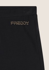 Tessuto nero con logo "FREDDY" decorato da borchie dorate vicino all'elastico in vita, che mostra parte della cucitura laterale del capo e dell'area della tasca.