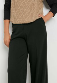 Brede zwarte broek met een gladde textuur, gecombineerd met een lichtgekleurd beige kabelgebreide trui met een ruitpatroon.