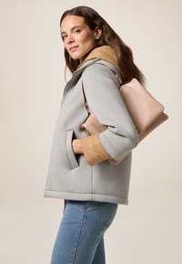 Felpa grigia con cappuccio e polsini trapuntati color beige, abbinata a una borsa a tracolla rosa chiaro con texture. Jeans slim completano il look.