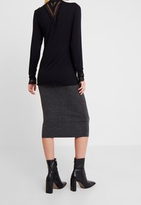 Svart långärmad topp med spetsdetaljer på baksidan, tillsammans med en grå rippad midikjol och svarta klackiga ankelskor.