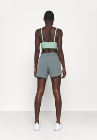 Sostenedor deportivo verde menta con tirantes ajustables, combinado con pantalones cortos atléticos grises que cuentan con una cintura ajustable y una textura ligera y suave.