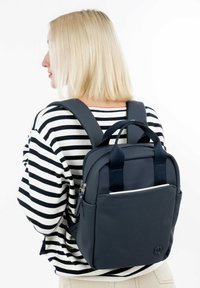 Námořnický batoh vyrobený z odolného materiálu, s dvojitými horními madly, nastavitelnými popruhy a přední kapsou s bílým zipem.