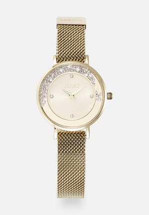Gullfarget klokke med rund urskive som har glitrende detaljer rundt skiven, mesh-reim og minimalistiske timeindikatorer.