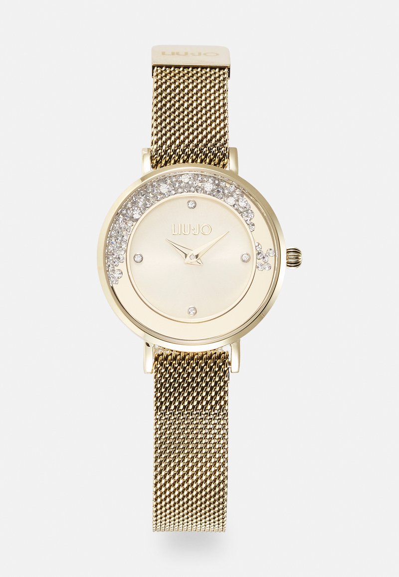 Montre dorée avec un cadran rond ornée d'accentuations scintillantes autour du cadran, bracelet en maille et marqueurs d'heures minimalistes.
