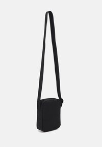 Bolso bandolera negro de forma rectangular, hecho de material suave, con una correa larga y ajustable y un cierre de cremallera.