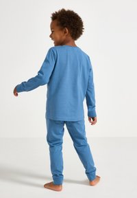 Langärmliges Hemd aus blauer Baumwolle und passende Hose, mit lockerer Passform und gerippten Bündchen, von hinten an einem Kind präsentiert.
