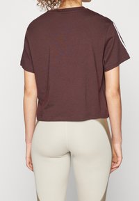 Brun kortärmad t-shirt i cropped-modell. Mjuk bomullstyg, rund halsringning och en enkel baksida. Matchas med ljusbeiga leggings med sidoseamsdesign.