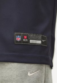 Tengeri kék mez, NFL és NFLPA logókkal, fekete címke a "Bajnok sportolók pontos specifikációinak megfelelően tervezve" felirattal, szürke melegítőnadrág fehér Nike logóval.