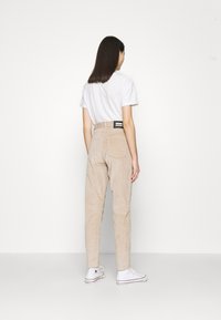 Beige kordbyxor med hög midja, med en svart etikett på baksidan, i kombination med en vit t-shirt och vita sneakers.