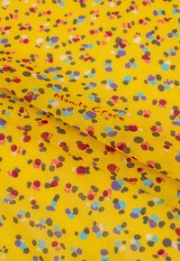 Tessuto giallo con punti multicolori in rosso, blu, grigio e viola. Texture morbida con branding stampato "Manila Grace."