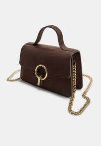 Sac à main en suede marron avec chaîne dorée, fermoir circulaire en métal et anse supérieure. Forme rectangulaire compacte avec une texture lisse et un minimalisme dans les détails.