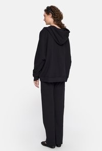 Czarna bawełniana bluza z kapturem, z kieszenią kangurzą i oversize'owym krojem, w zestawie z dopasowanymi szerokimi spodniami. Gładka tekstura, minimalistyczny design.