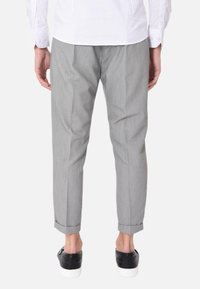 Pantaloni grigi a sigaretta con motivo a righe sottili, orlo con risvolto e pieghe frontali, abbinati a sneakers nere, visti da dietro.