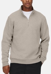Jasnoszary sweatshirt z zamkiem przy kołnierzu, ściągaczami przy mankietach i u dołu. Wykonany z miękkiej, teksturowanej tkaniny, charakteryzujący się luźnym krojem i minimalistycznym wzornictwem.