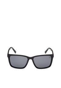 Lunettes de soleil rectangulaires noires avec verres teintés foncés et branches courbées, présentées sur un fond blanc.