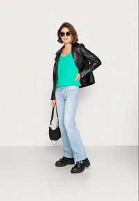 Jaqueta de couro preta, top verde, jeans azul claro e sapatos de plataforma pretos. Acessório: pequena mala preta e óculos de sol.