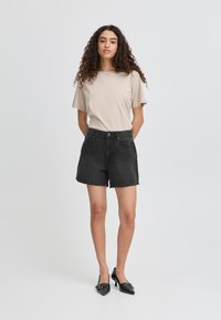 T-shirt beige à manches courtes, associé à un short en denim noir taille haute. Des escarpins noirs à bout pointu complètent la tenue.