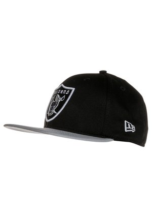 Gorra de béisbol negra con visera gris, que presenta un logo de los Raiders en blanco cosido en la parte delantera y un logo más pequeño en el lateral.