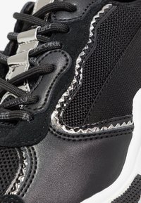 Black sneaker featuring mesh, suede, and smooth leather materials. Notable silver accents and textured patterns along the sides.
