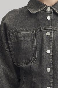 Denim jacket in grey with a collar, silver snap buttons, and a large chest pocket. Textured fabric with stitching details.