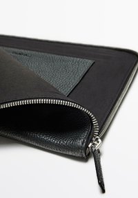 Schwarze Ledertasche mit strukturiertem Oberflächen, ausgestattet mit einem silbernen Reißverschluss, glatter Fütterung und einem separaten Innentaschen-Detail.