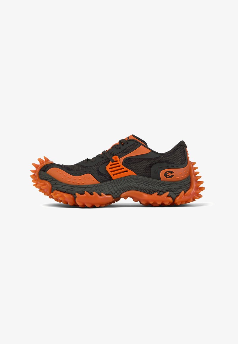 Schwarz-orangefarbener Sportschuh mit dicker, strukturierter Sohle und großen, stacheligen Profilen im Zehen- und Fersenbereich.