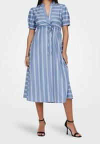 Blå randig midiklänning med korta puffärmar, djup V-ringning, justerbart knytmidja och en flödande kjol. Svarta klacksandaler fulländar outfiten.