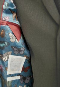 Dark green suit with a silk inner lining featuring a blue background and colorful butterfly and insect patterns. Includes a patch pocket.