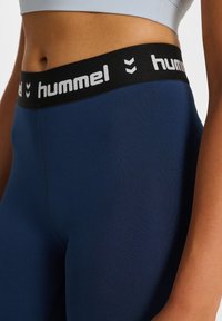Marina leggings med svart elastisk midja som har vit "hummel" text och chevron-mönster; slät textur och åtsittande passform.