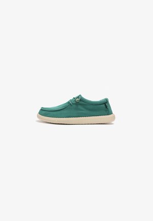 Botte slip-on en toile verte avec semelle en caoutchouc beige, présentant un bout arrondi, des détails en dentelle décoratifs et des accents cousus sur le dessus.