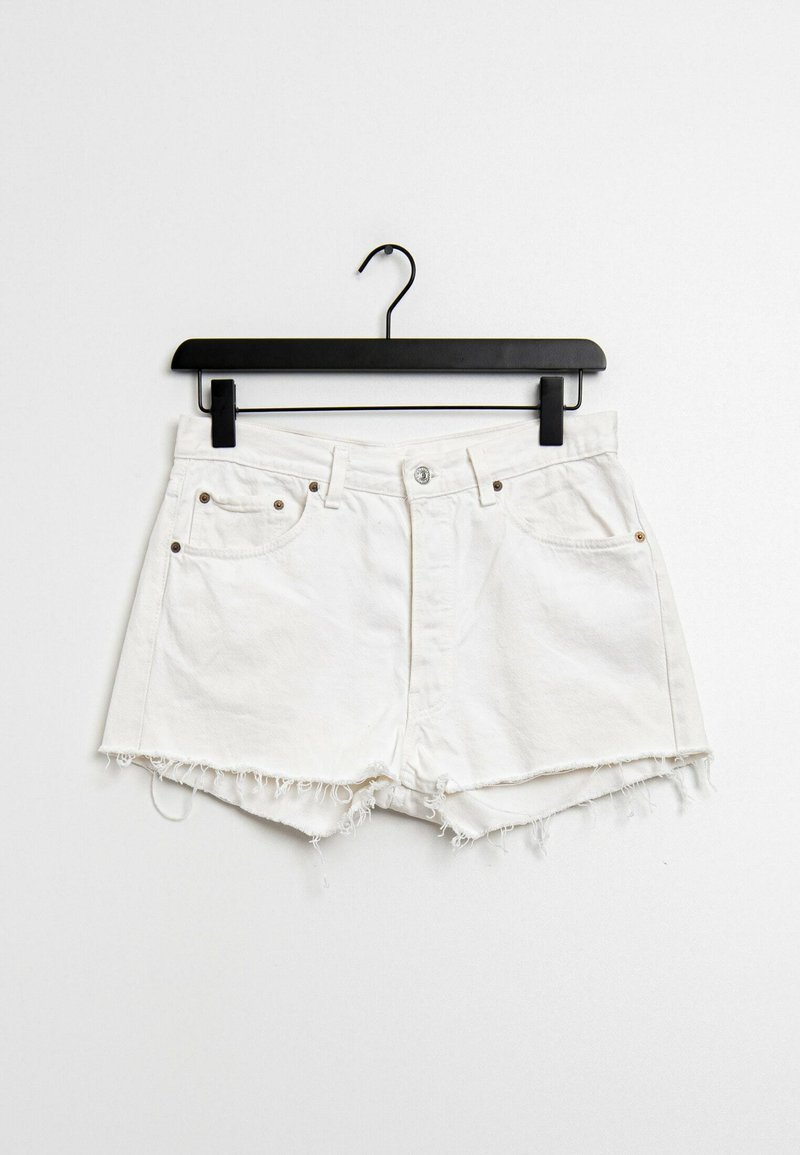 Pantalones cortos de mezclilla blanca con dobladillo deshilachado, diseño de cinco bolsillos, herrajes metálicos y cierre con botón, colgando de una percha negra.