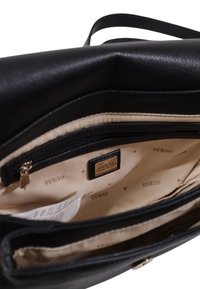 Borsa a mano in pelle nera con una superficie liscia, dotata di una fodera interna beige chiaro. Include una tasca con zip e un'etichetta del marchio ben visibile.