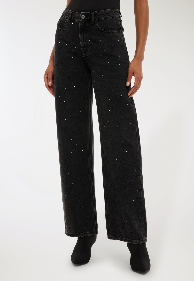 Czarne spodnie dzwony z wysokim stanem, ozdobione małymi srebrnymi ćwiekami rozsianymi po tkaninie. Wykonane z denimu o miękkiej fakturze.