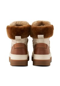 Białe i brązowe botki z kołnierzem z sztucznego futra, wykonane ze skóry, z masywną białą podeszwą oraz detalem z logo z tyłu. Teksturowane akcenty na całej powierzchni.