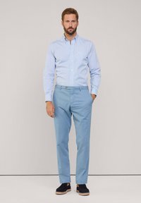 Pantalones de algodón azul claro con una textura suave, combinados con una camisa a rayas azul claro y blanca. Zapatos negros con una suela texturizada.