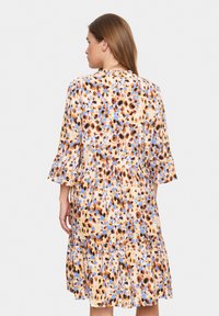 Robe fleurie avec un fond beige ornée de motifs floraux orange et bleu. Elle a des manches évasées et un design de jupe à volants.