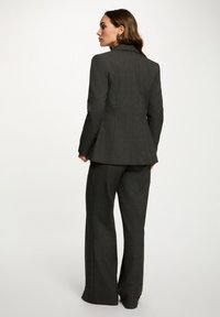 Completo su misura a quadri grigi con blazer sagomato e rever a punta e pantaloni a gamba larga, che mette in mostra un design strutturato e una superficie liscia.