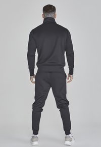 Chándal deportivo negro con cuello alto, diseño ajustado y puños acanalados. Textura suave sin patrones ni acentos visibles.