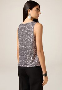 Bezrękawnik z błyszczącym, srebrnym wzorem z cekinów; dopasowany fason; gładka faktura; zestawiony z czarnymi spodniami.