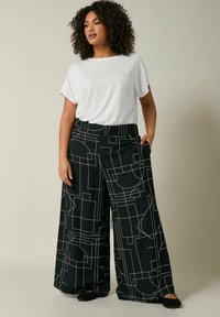 Pantaloni a gamba larga neri con un motivo geometrico astratto bianco. Abbinati a una t-shirt bianca a vestibilità comoda. Tessuto morbido.