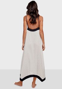 Largo vestido blanco con tirantes finos, que presenta un ribete de satén negro en el escote y el dobladillo. La tela tiene una sutil textura con un patrón.