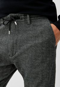 Grå mønstrede bukser med en tekstureret stof, snor i taljen og frontlommer. Har metallic hardware-detaljer til justering.