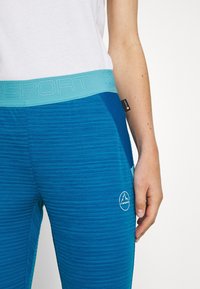 Blue athletic pants with a textured pattern and a breathable turquoise waistband. Features a white logo on the lower leg.